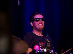 junger Mann mit Sonnenbrille und breitem Grinsen am Schlagzeug