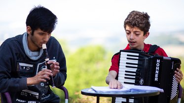 Zwei Jungen mit Blockflöte und Akoordeon, ein Junge deutet helfend auf die Noten