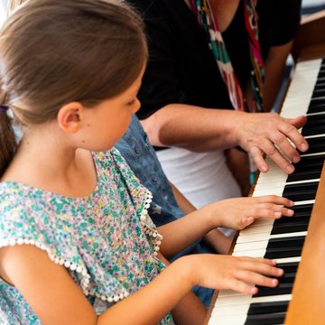 Kinderhände auf einer Klaviertastatur, daneben die Hand einer erwachsenen Person