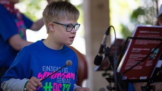Junge mit Downsyndrom spielt Xylofon. Auf seinem T-Shirt steht Einzigartig, gemeinsam genial, FIS 2017