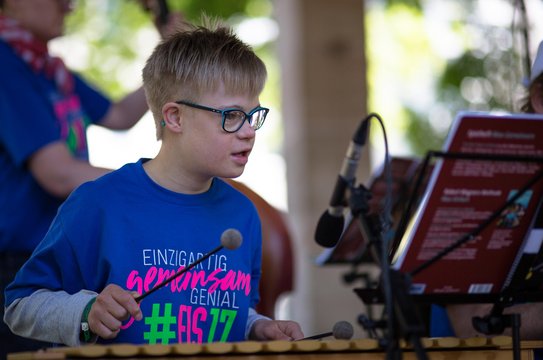 Kleiner Junge mit Down-Syndrom spielt Xylofon und schaut konzentriert in die Noten