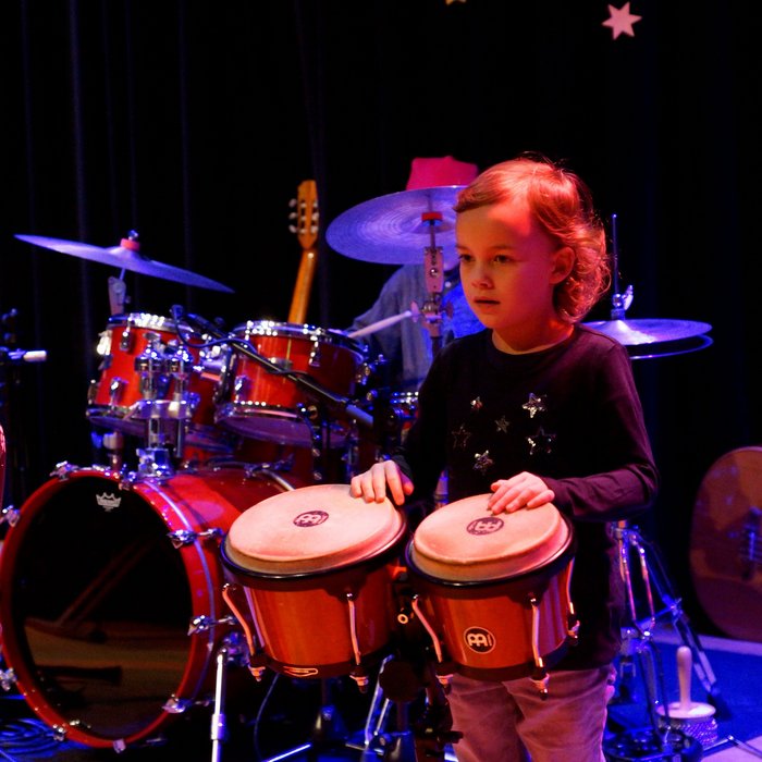 Mädchen im Grundschulalter spielt Bongos, Schlagzeug im Hintergrund