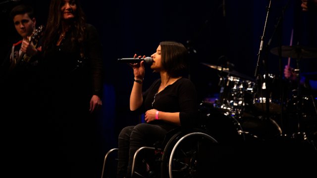 Eine Sängerin im Rollstuhl singt mit geschlossenen Augen
