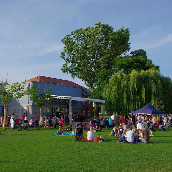 Wiese im Südstadtpark, auf der Open-Air-Bühne spielt eine Band, Menschen picknicken im Sonnenschein