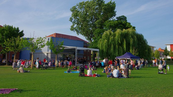 Sommer im Südstadtpark: auf der Open Air Bühne spielt eine Band, auf der Wiese sitzen viele Menschen
