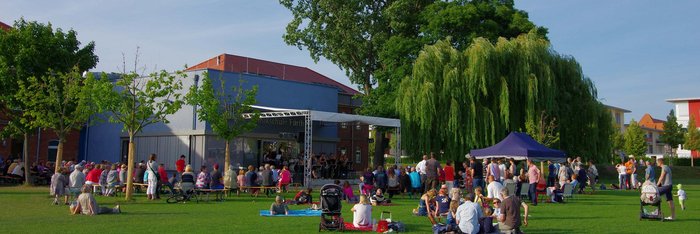 Sommer im Südstadtpark: auf der Open Air Bühne spielt eine Band, auf der Wiese sitzen viele Menschen