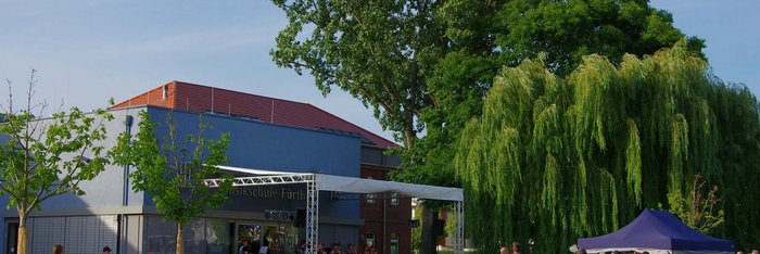 Wiese im Südstadtpark, auf der Open-Air-Bühne spielt eine Band, Menschen picknicken im Sonnenschein
