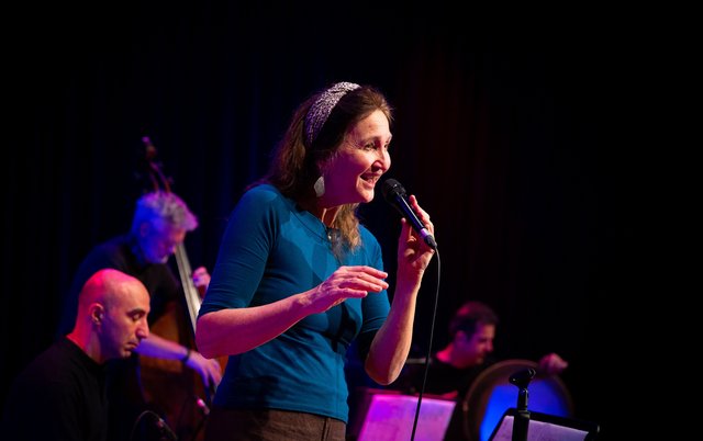 Gesangsdozentin Susanne Schönwiese mit Mikro, im Hintergrund die Band