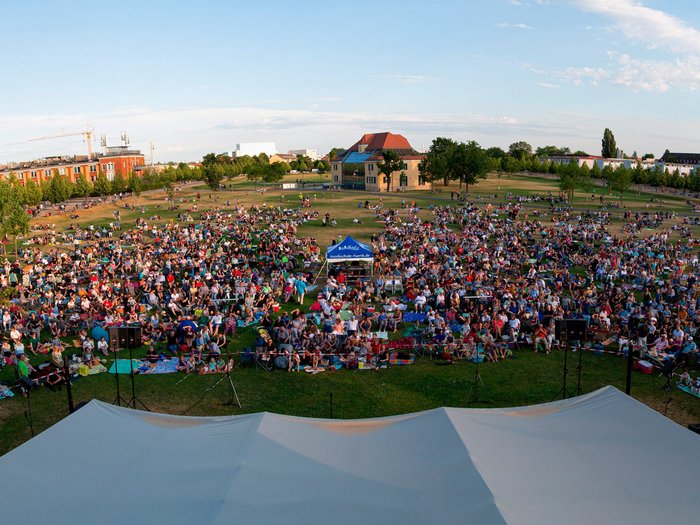 Blick vom Dach der Musikschule in den Südstadtpark. Viele Menschen sitzen bei einem Open Air Konzert auf der Wiese