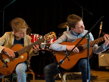 Zwei Jungen spielen Gitarre auf einer Bühne, im Hintergrund steht ein Schlagzeug