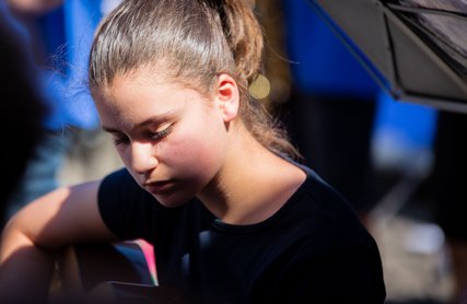 Mädchen spielt Gitarre, sie ist im Freien, ihr Gesicht liegt zur Häfte im Schatten
