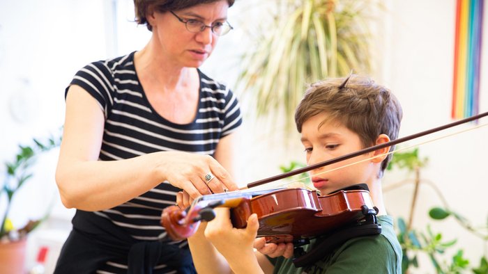 Junge mit Geige, Lehrerin zeigt ihm die Bogenhaltung der Geige