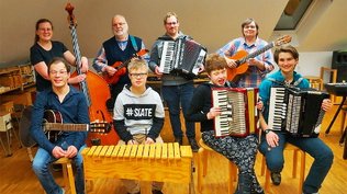 Ein Gruppenfoto des Ensembles Patchwork: Menschen mit Behinderung mit Akkordeon, Gitarre, Xylofon, Ukulele, Kontrabass
