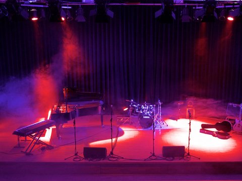 Bühne mit Schlagzeug, Flügel, Keyboard und einem Gitarrenkasten in rotem Scheinewrferlicht