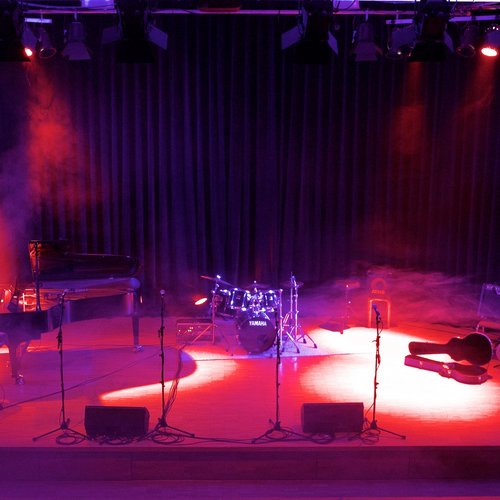 Bühne mit Schlagzeug, Flügel und geöffnetem Gitarrenkasten im roten Scheinwerferlicht
