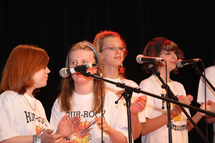 Vier Mädchen in weißen T-Shirts singen, vor ihnen stehen MikrosMusikschule Fürth