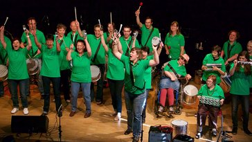Die Fürther Sambistas in grünen T-Shirts auf der Bühne, zwei Musikerinnen sitzen im Rollstuhl. 
