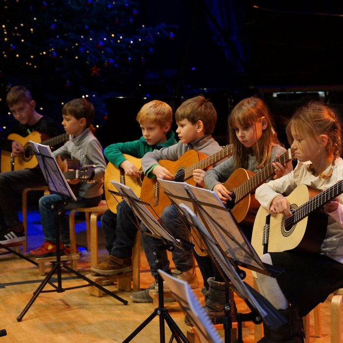 Gitarrenkinder im Grundschulalter sitzen nebeneinander auf der Bühne