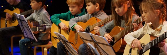 Gitarrenkinder im Grundschulalter sitzen nebeneinander auf der Bühne