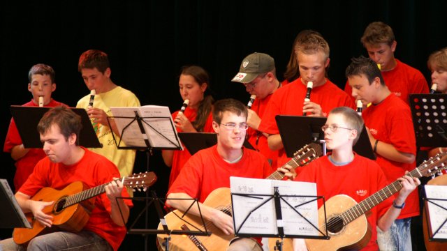 Mehrere Musiker:innen mit Blockflöten und Gitarren in roten T-Shirts auf der Bühne