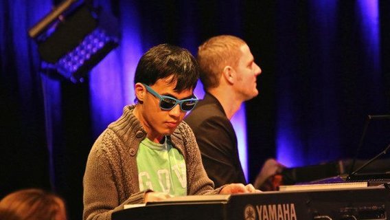 Junger Mann mit blauer Sonnenbrille spielt E-Piano